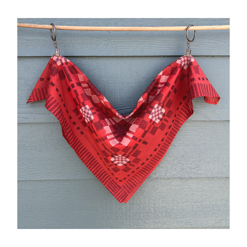 Vibrant red patterned bandana with a modern patchwork design, draped over a  clothesline