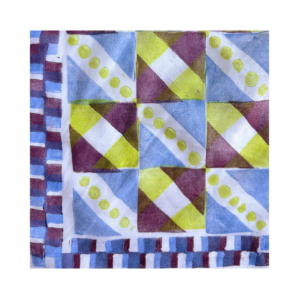 A detail of a bandana with a geometric patchwork pattern in blue, green, yellow, and brown, finished with a checkered border. 