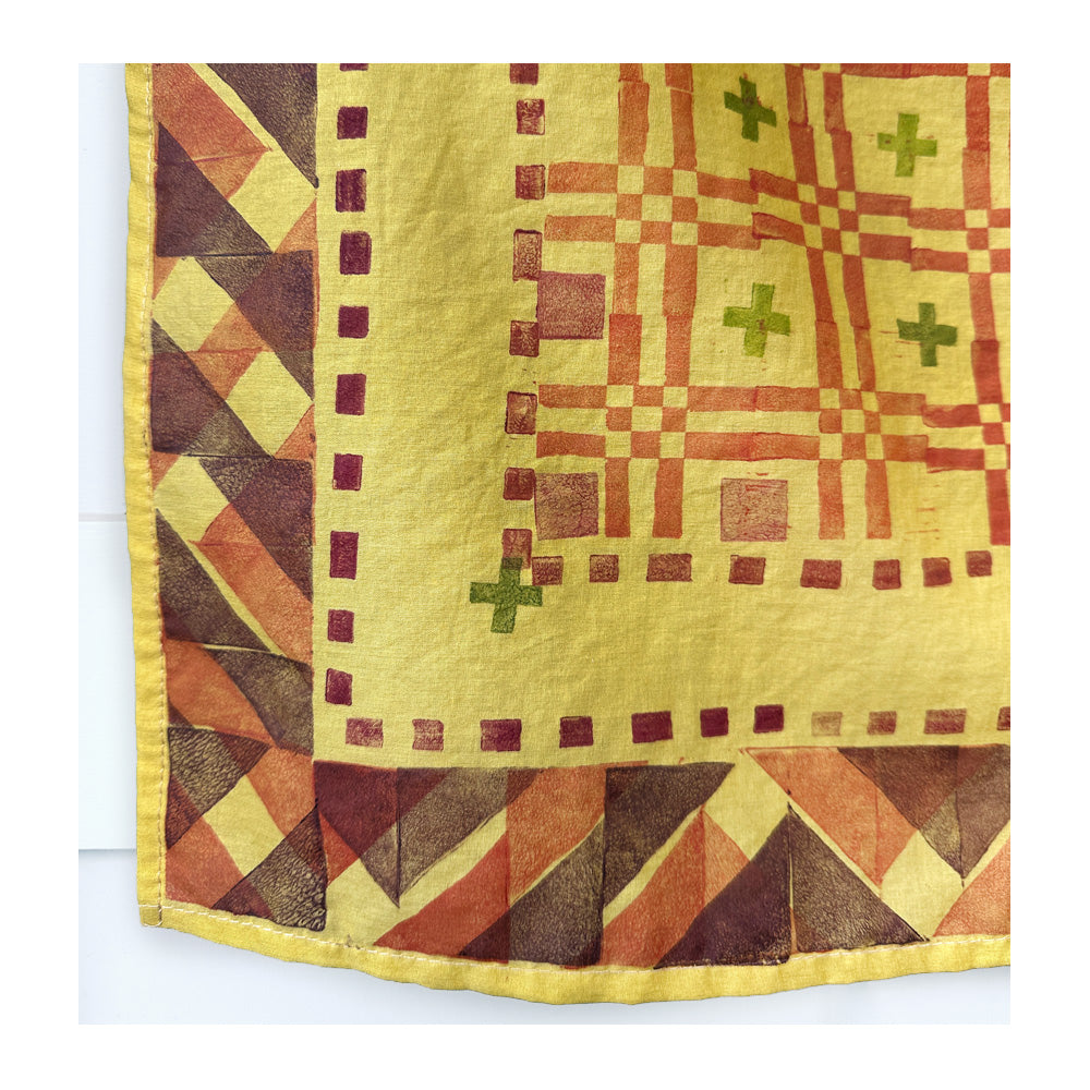 Close up detail photo of a hand-printed sunny yellow bandana with a boxy geometric pattern on a white background
