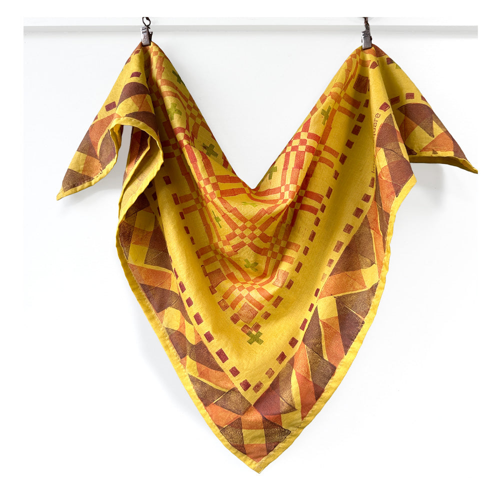 Warm yellow geometric patterned bandana draped over a white background 