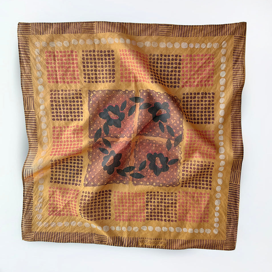 Ochre colored bandana with a dot and check pattern and a floral motif at center